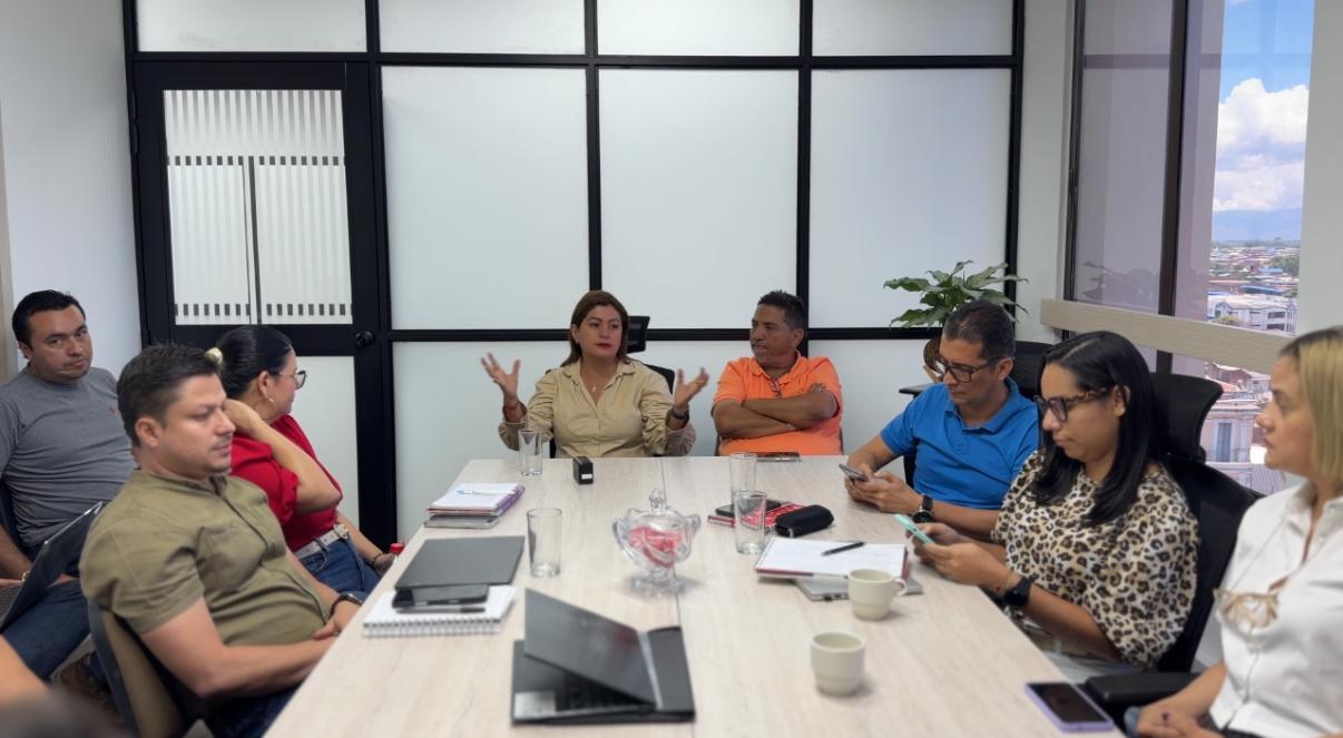 Grupo diverso de profesionales y ciudadanos en una mesa de trabajo técnica, analizando situacion de recolección de basuras frente a una pantalla con logotipos institucionales en la Alcaldía de Palmira.