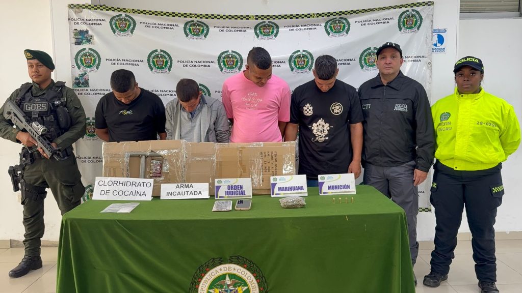 Fotografía oficial de la Policía Nacional de Colombia mostrando a cuatro hombres capturados y elementos incautados sobre una mesa, custodiados por oficiales de diferentes unidades.