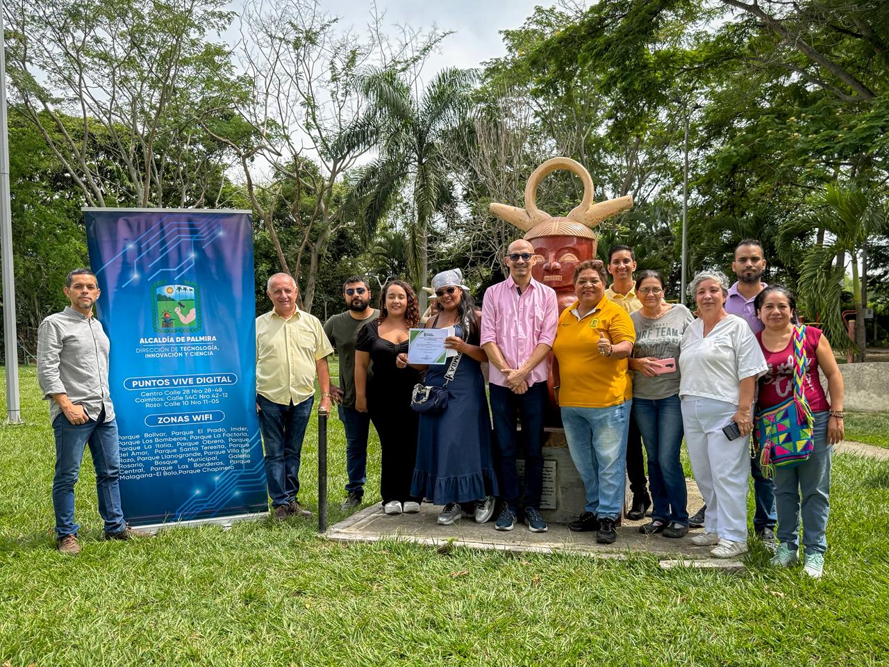 Grupo de personas en El Bolo San Isidro de Palmira posando junto a una escultura de rostro precolombino y un pendón de zonas Wifi Gratuitas. Una mujer en el centro sostiene un certificado de entrega zona WiFi