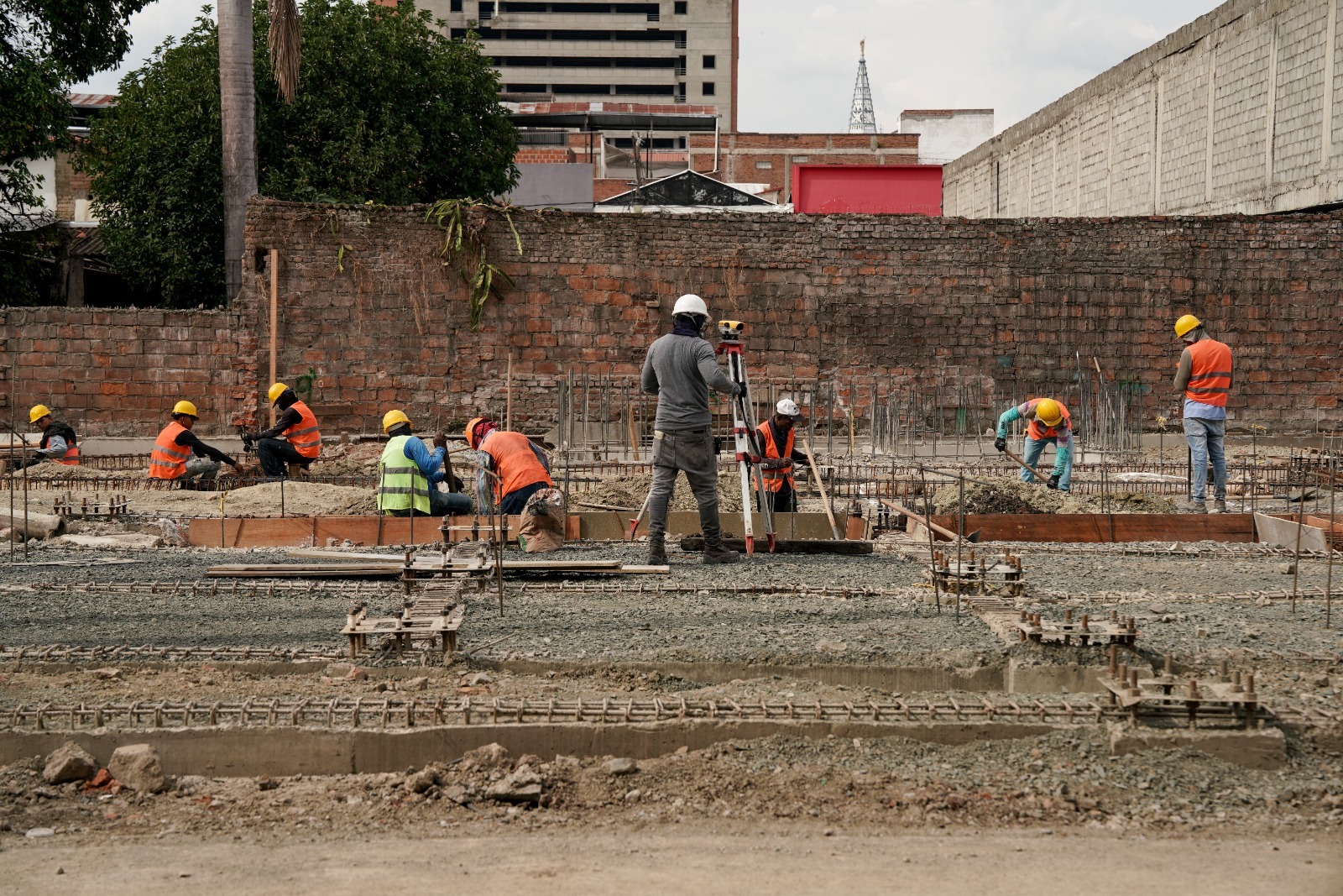 Un equipo de personal de obra, con cascos y chalecos reflectantes, trabaja en la cimentación de una construcción en la Galería de Palmira. En el centro, una persona utiliza un nivel topográfico para medir el terreno.