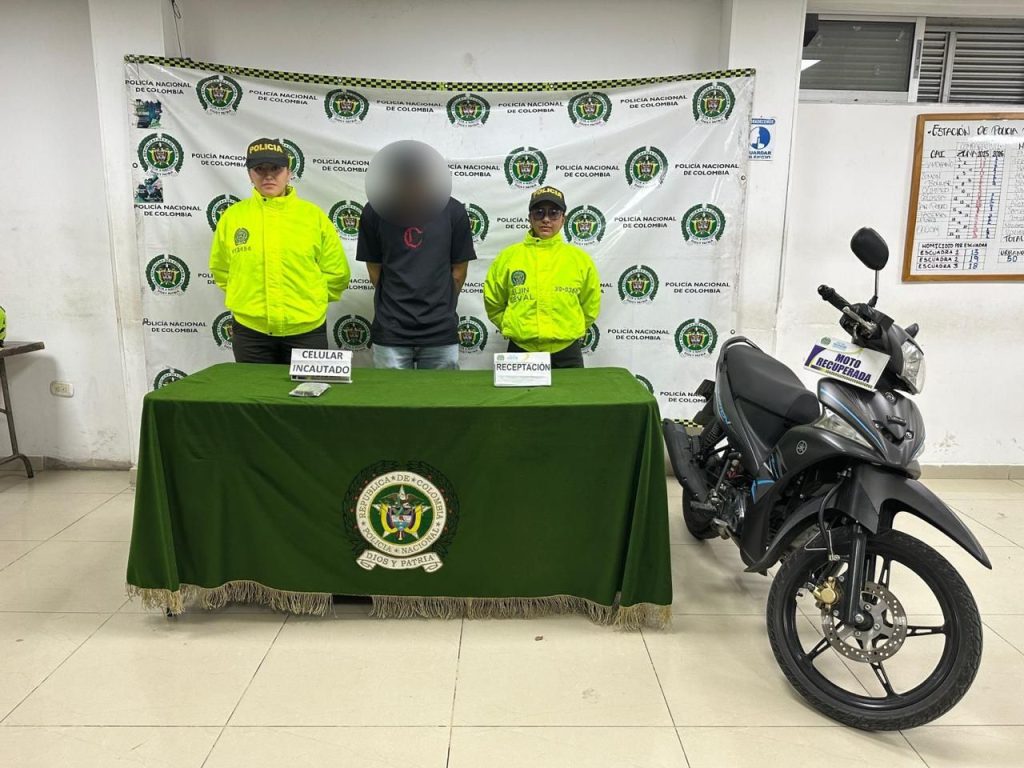 Personal de la Policía Nacional de Colombia junto a una persona detenida y elementos recuperados, incluyendo una motocicleta y un celular.