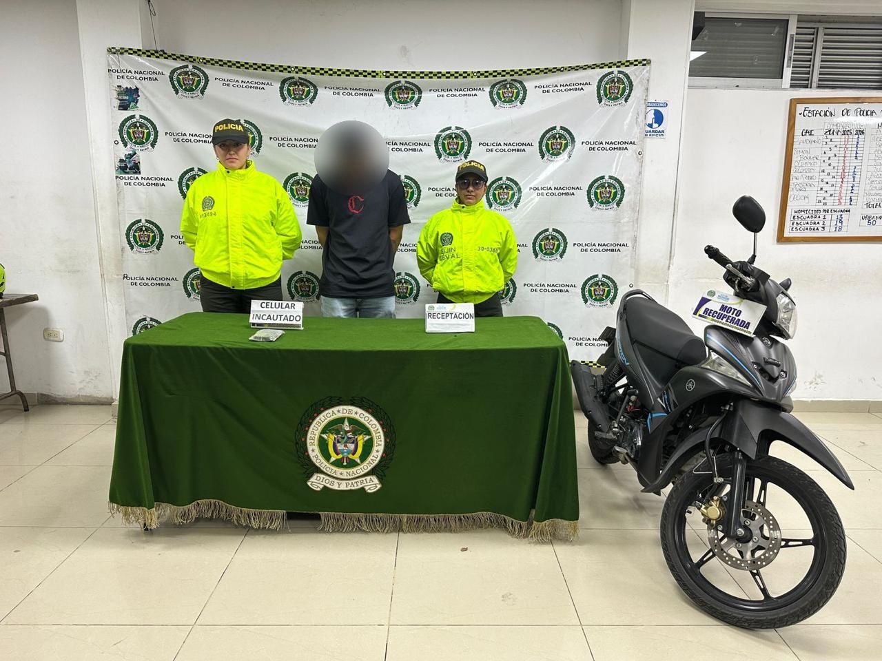 Personal de la Policía Nacional de Colombia junto a una persona detenida y elementos recuperados, incluyendo una motocicleta y un celular.