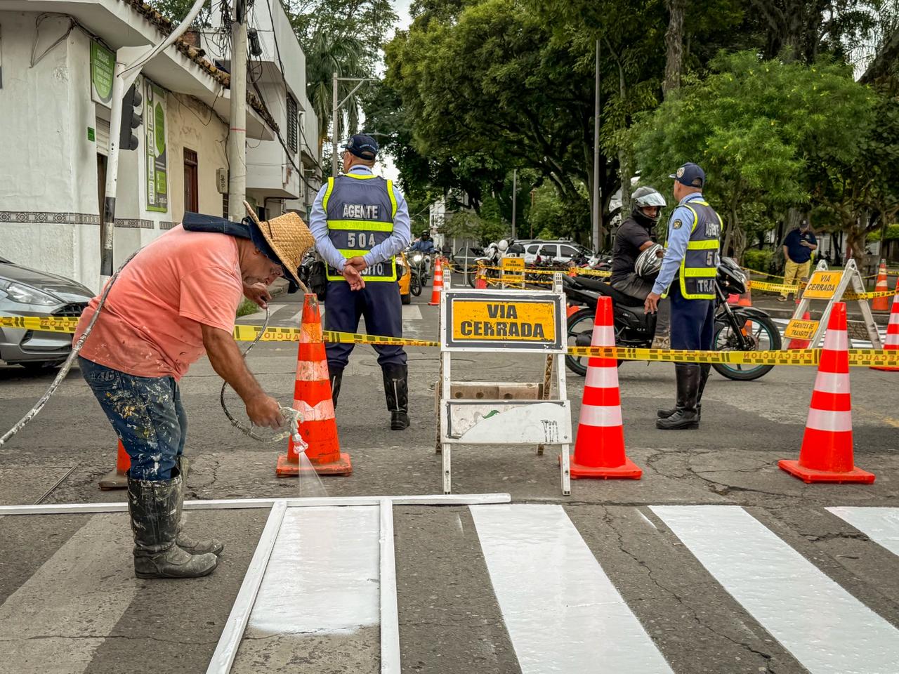 Personal operativo realiza el mantenimiento de la señalización vial pintando un paso peatonal en una calle de Palmira. Al fondo, agentes de tránsito supervisan el cierre de la vía
