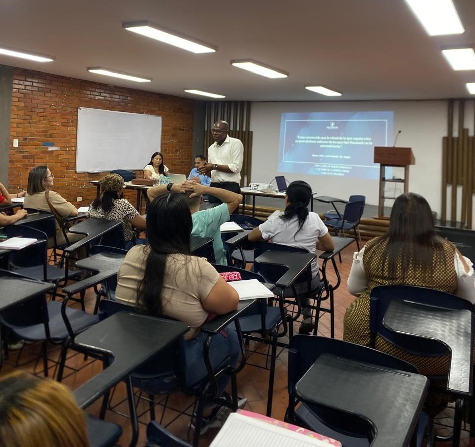 Un grupo de personas en un aula sigue la presentación de un ponente frente a una pantalla de proyección.