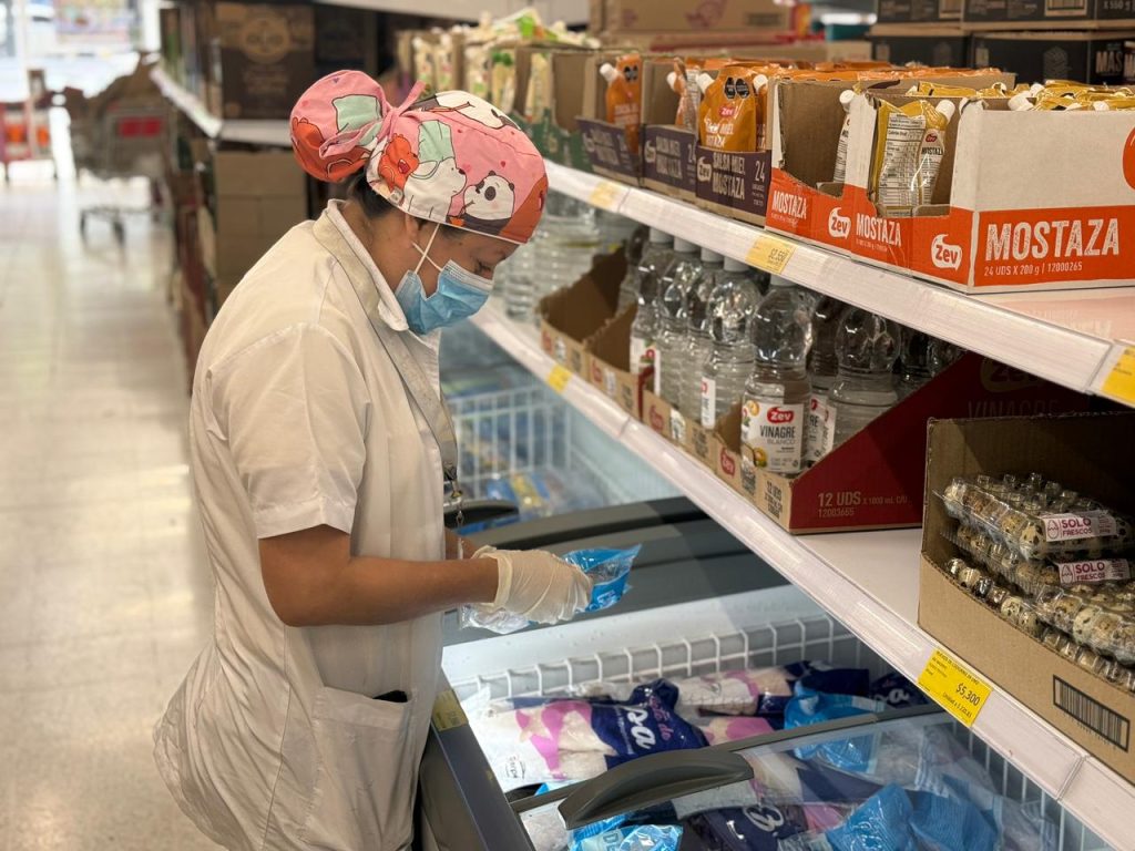 Integrante del equipo de salud pública, con uniforme blanco, mascarilla y guantes, inspecciona productos en un congelador de supermercado en Palmira