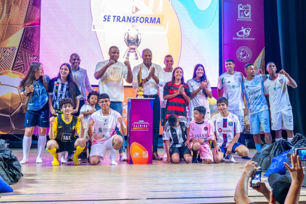 Grupo de jóvenes y con alcalde Víctor Ramos adultos con camisetas de fútbol celebrando junto a un trofeo en un escenario oficial