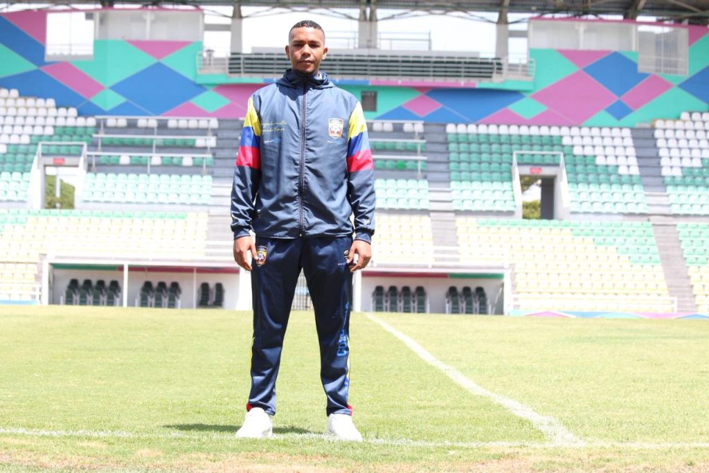 Retrato de pie de un hombre joven afrodescendiente, deportista con un uniforme deportivo de los colores de Colombia, en el centro de la cancha de césped del Estadio Francisco Rivera Escobar en Palmira