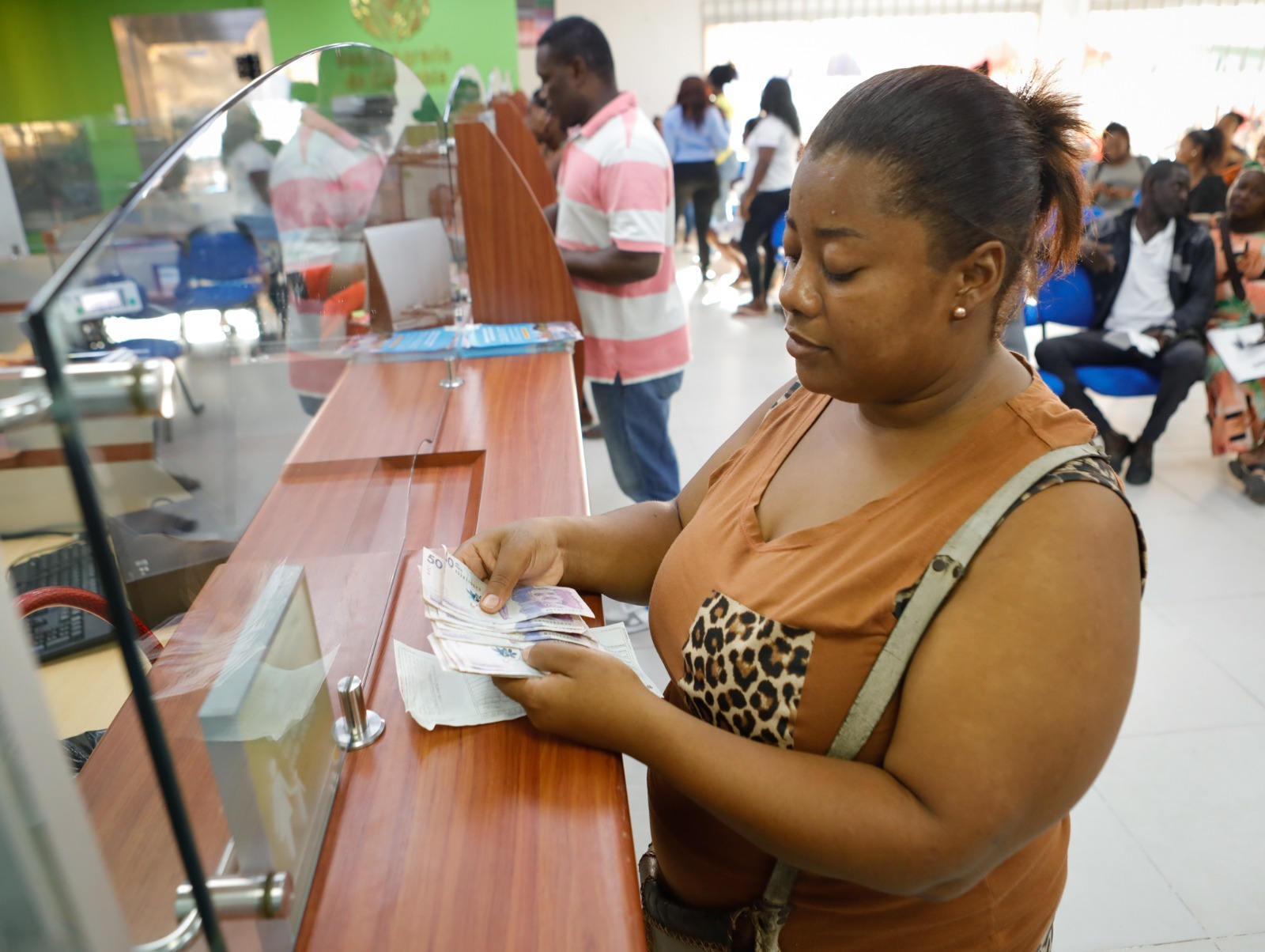 Una mujer cuenta billetes frente a una ventanilla de atención al cliente en una oficina pública o bancaria
