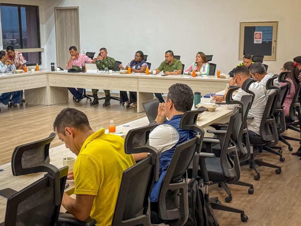 Reunión de un equipo de trabajo diverso en una mesa en forma de U, con participación de personal civil y militar en un entorno institucional de la Alcaldía de Palmira