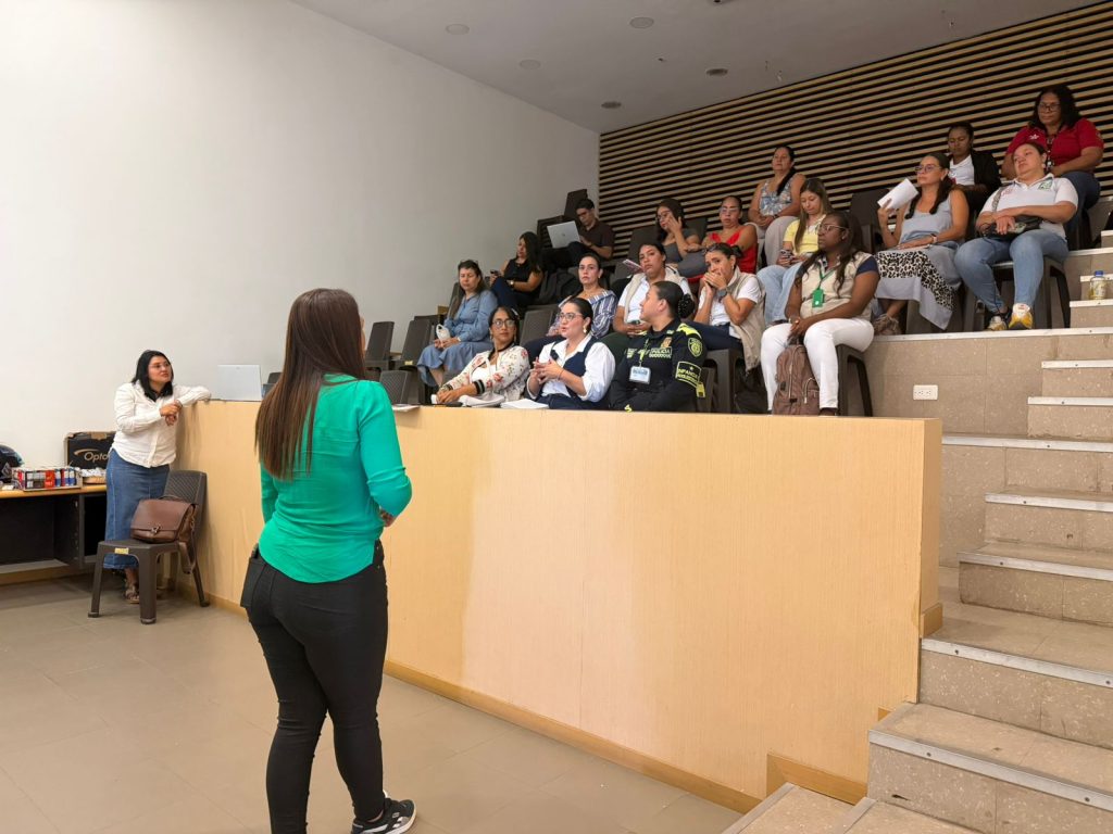 Una mujer de espaldas con blusa verde habla ante una audiencia sentada en un auditorio escalonado. El grupo de asistentes al CIETI Palmira incluye a personal civil y a una oficial de la Policía Nacional de Colombia.