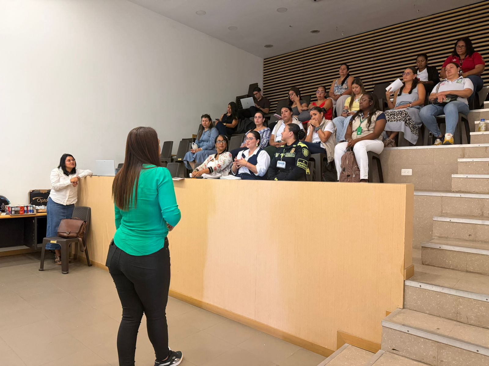 Una mujer de espaldas con blusa verde habla ante una audiencia sentada en un auditorio escalonado. El grupo de asistentes al CIETI Palmira incluye a personal civil y a una oficial de la Policía Nacional de Colombia.