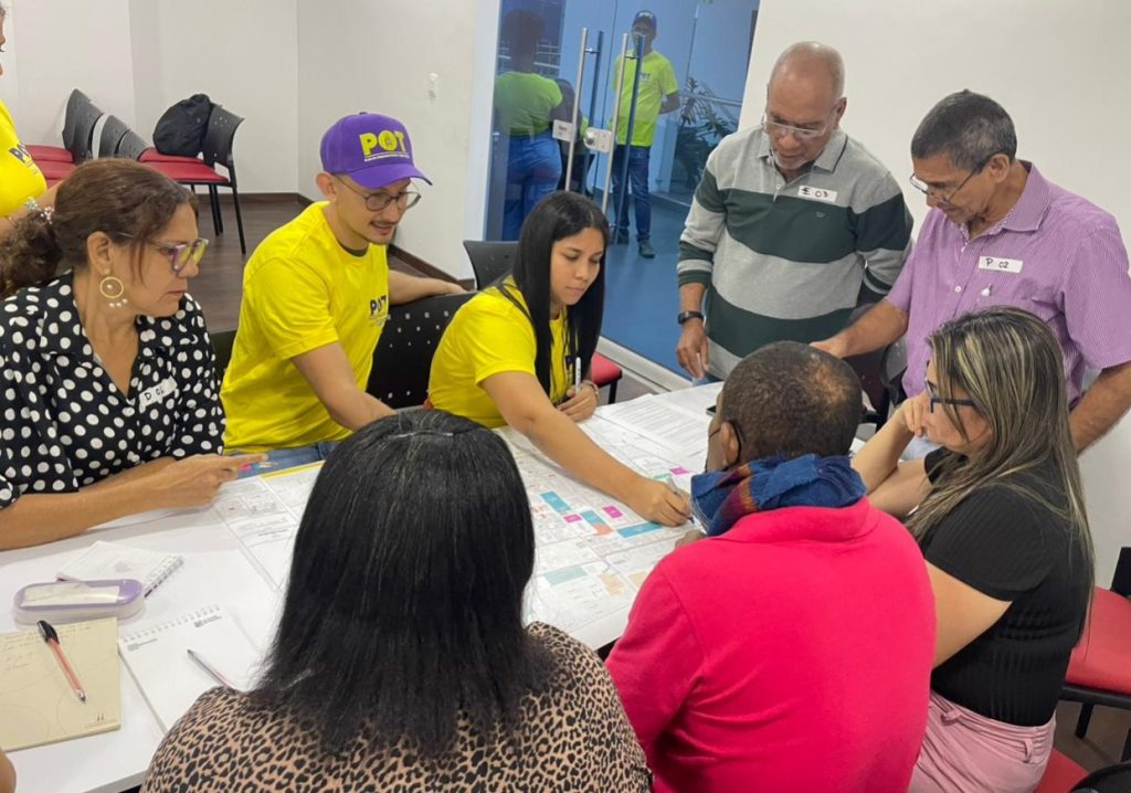 Un grupo de personas reunidas alrededor de una mesa de trabajo analizan un mapa técnico o plano a gran escala con anotaciones de colores.