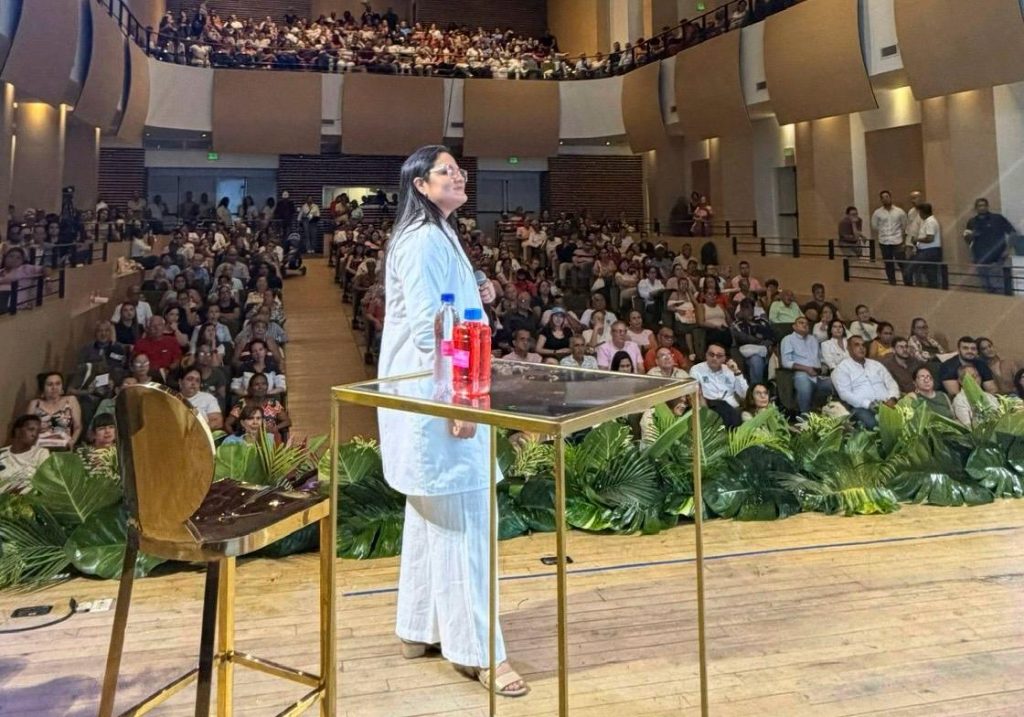 Gerente Hospital Raul Orejuela con anteojos y ropa blanca habla desde el escenario ante un auditorio lleno.
