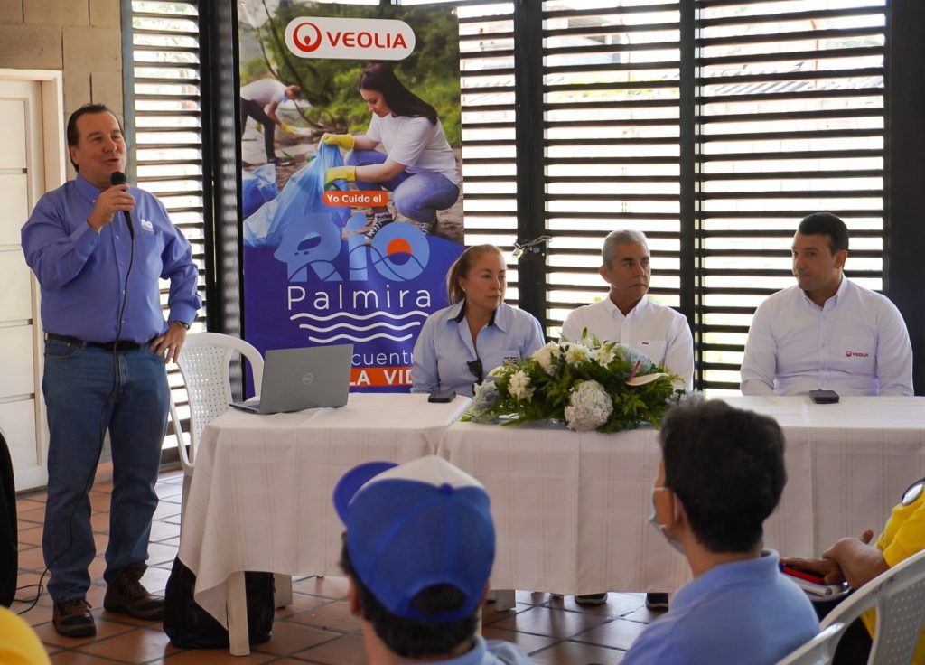 Evento con directivos de empresas de servicios públicos, hombre habla por micrófono junto a una mesa con directivos. El evento cuenta con la participación de la comunidad y representantes institucionales