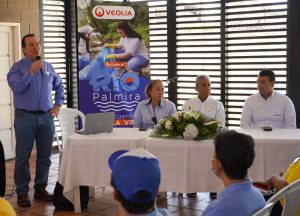 Evento con directivos de empresas de servicios públicos, hombre habla por micrófono junto a una mesa con directivos. El evento cuenta con la participación de la comunidad y representantes institucionales