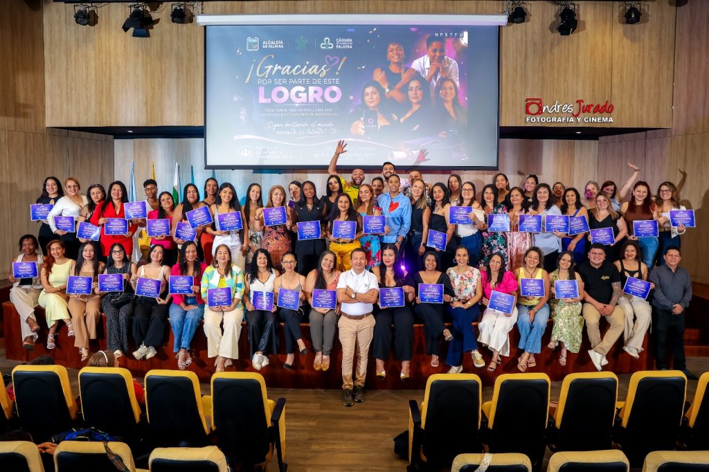 Un gran grupo de mujeres emprendedoras posa sonriente sosteniendo certificados azules en un auditorio frente a una pantalla que dice "¡Gracias! Por ser parte de este logro", junto a la Secretaria de Integración Social Catherine Filigrana