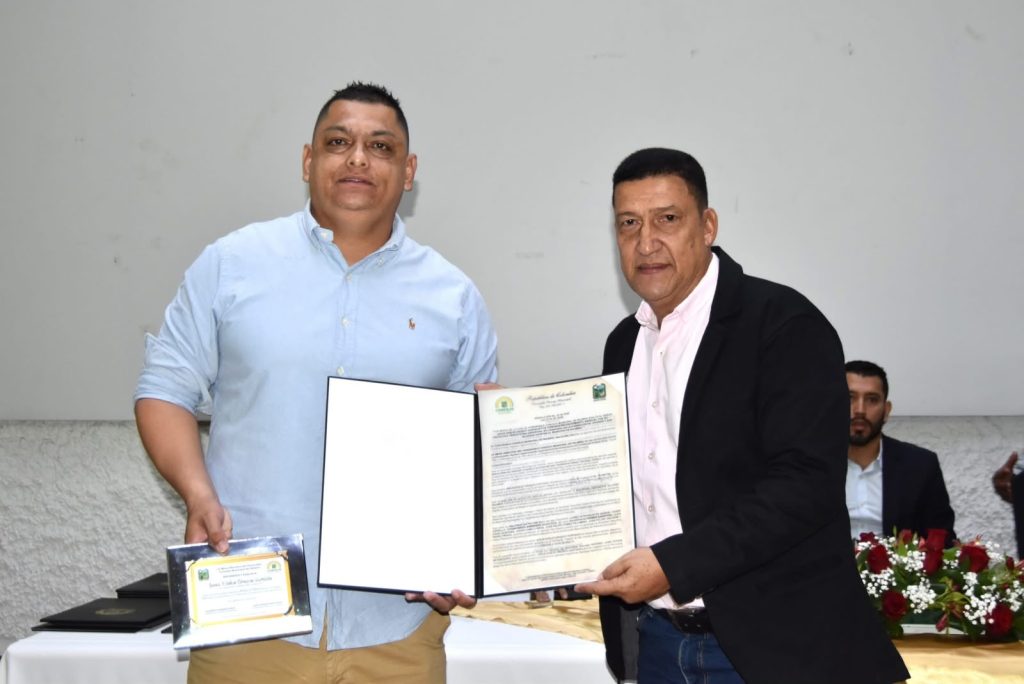 Fotografía institucional en el Concejo Municipal de Palmira. Dos personas sostienen un diploma de resolución en carpeta negra y una placa metálica de reconocimiento durante un acto protocolario de exaltación.