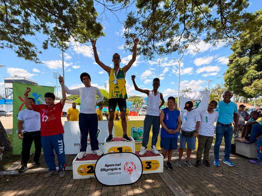 En a imagen tres atletas con medallas celebran en un podio de Special Olympics Colombia junto a organizadores y acompañantes al aire libre