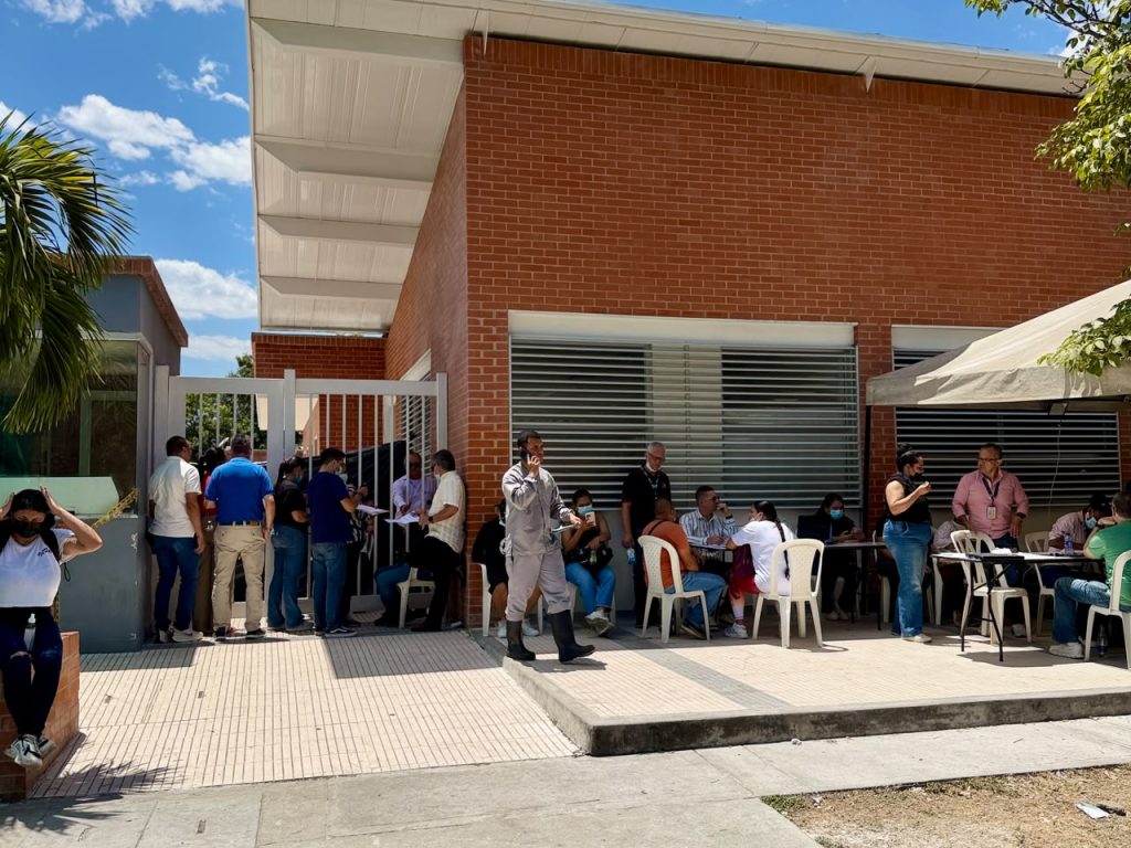 En la fotografía grupo de personas reunidas en las afueras de una edificación institucional durante una jornada espera