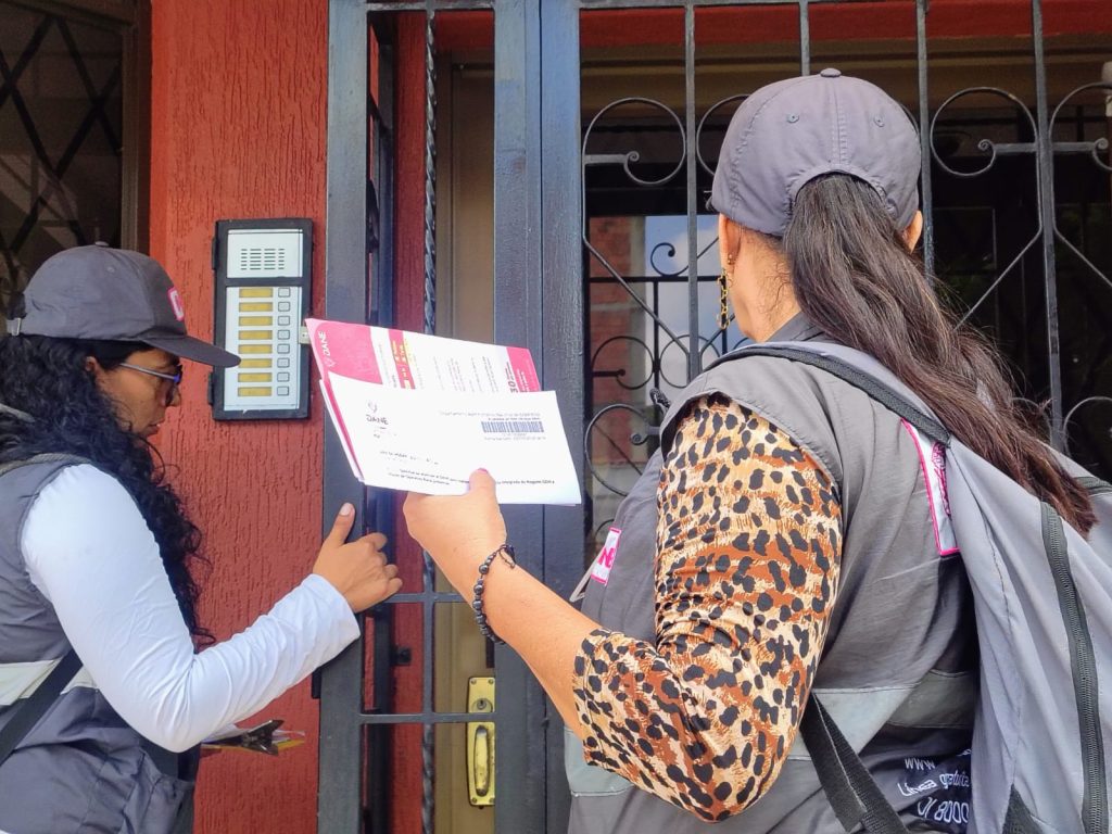 En la fotografía personal encuestador del DANE con gorra y chaleco institucional sosteniendo formularios de la Gran Encuesta Integrada de Hogares frente a la entrada de una vivienda en Palmira.