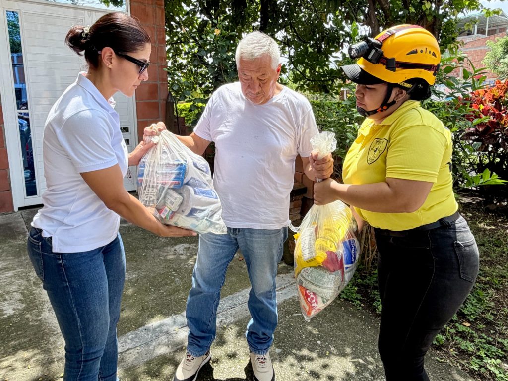 En la fotografía Dos integrantes de un equipo de atención entregan paquetes de víveres y kits de ayuda a un hombre adulto mayor.