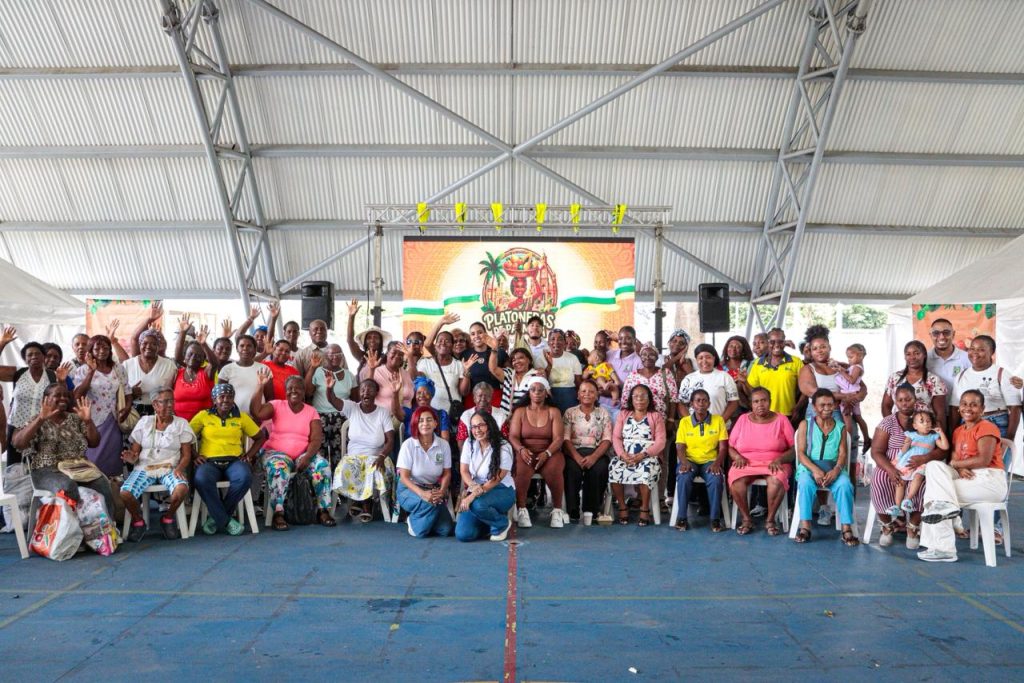 Fotografía grupal de mujeres platoneras afrodescendientes sonriendo y saludando en un evento comunitario bajo una estructura techada.
