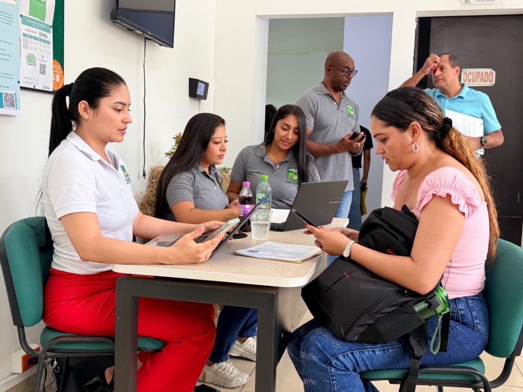 En la fotografía servidores públicos de la agencia de empleo atienden a una ciudadana en una mesa de orientación para el registro de su hoja de vida en la plataforma de empleo.