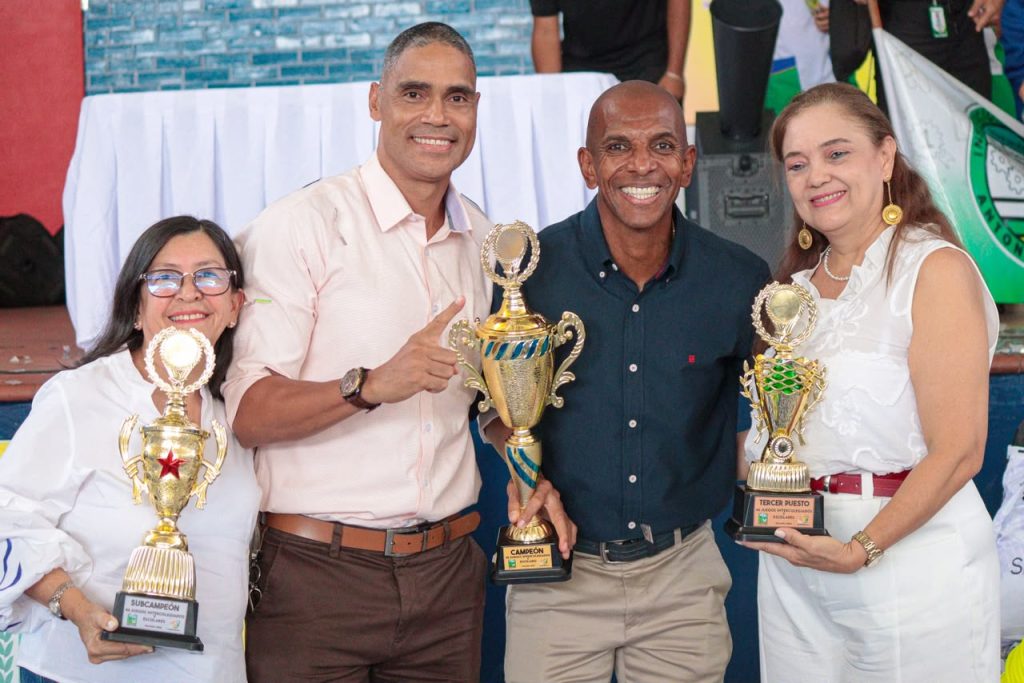 En la fotografía Dos mujeres y dos hombres posan sonrientes sosteniendo tres trofeos dorados de distintas categorías en un evento de premiación