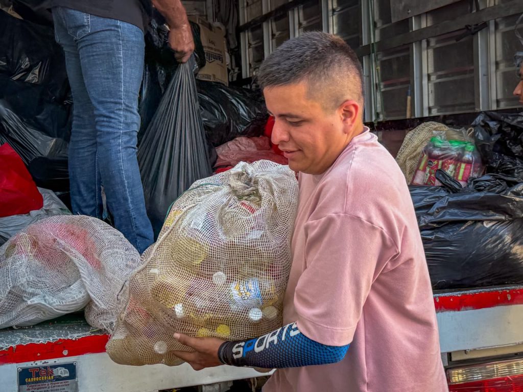 Una persona sonríe mientras carga un gran saco de malla lleno de alimentos no perecederos cerca de la parte trasera de un camión de carga.