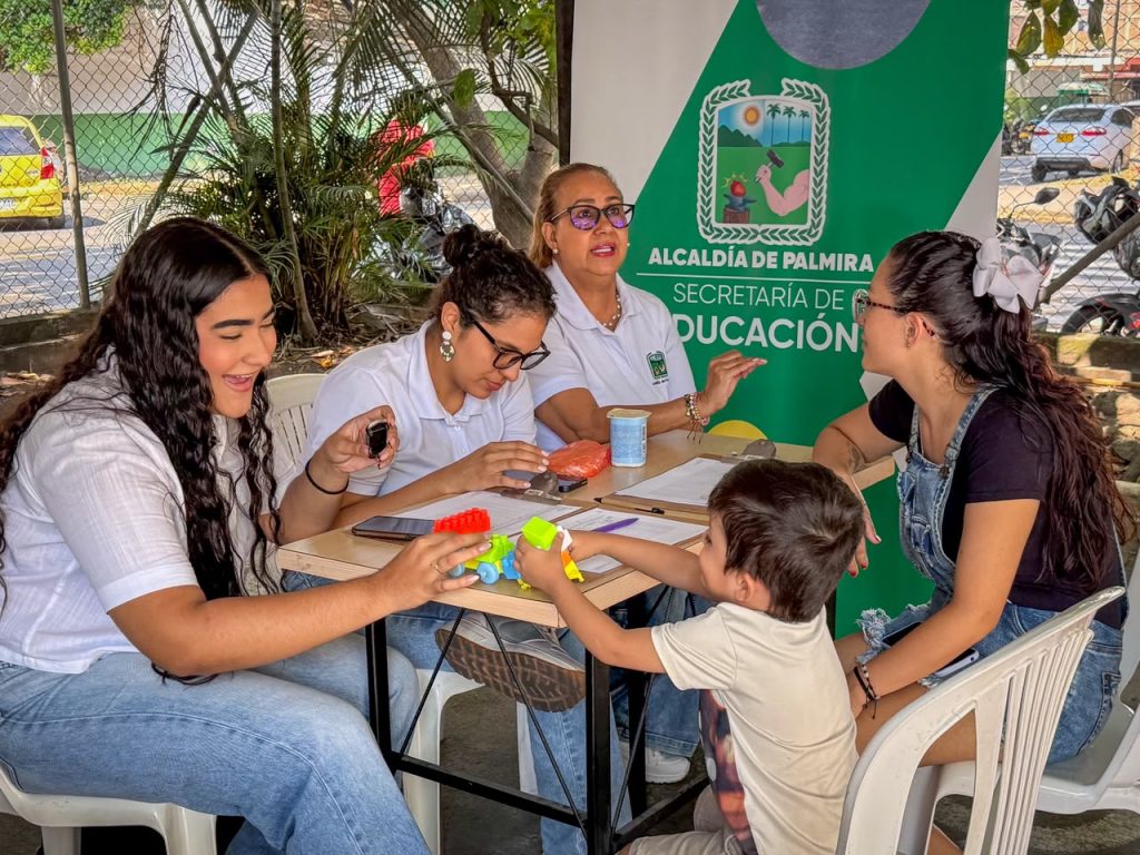 En la fotografia Dos integrantes de la Secretaría de Educación de Palmira atienden a un grupo de ciudadanas y un niño que juegan con bloques en una mesa