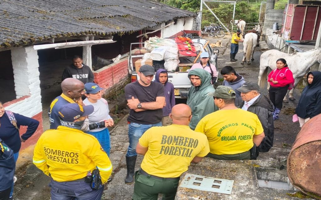 Integrantes del Cuerpo de Bomberos de Palmira con uniformes de brigada forestal reunidos con campesinos y miembros de rescate en un patio rural.