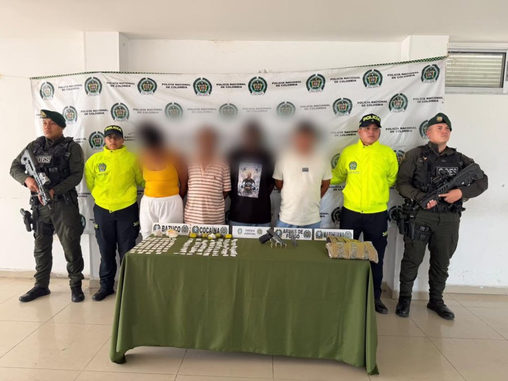 Cuatro personas capturadas con rostros difuminados escoltadas por agentes de la Policía Nacional, junto a una mesa con estupefacientes y armas incautadas.